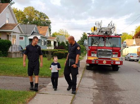 A boy and two firefighters walking on the street with a fire truck in the background. Property of Niagara Falls Review