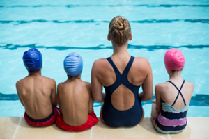 Four young students sit poolside with their instructor